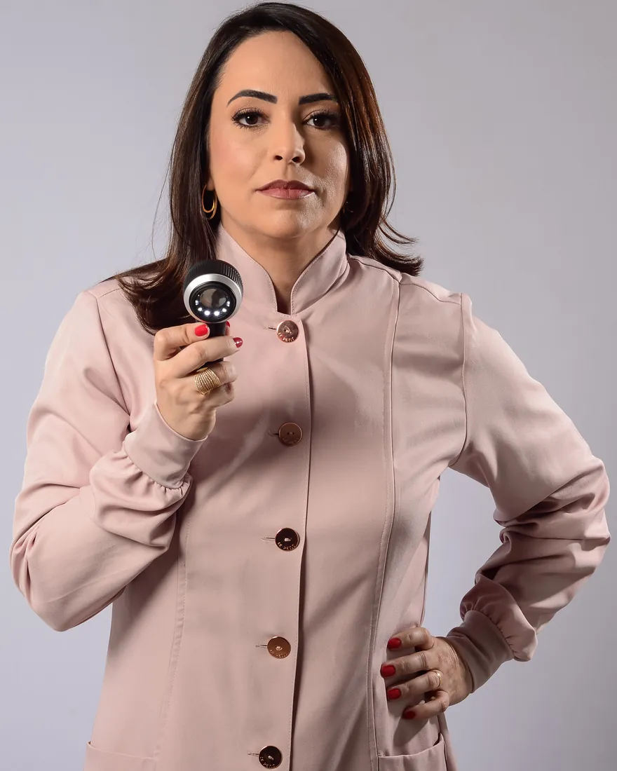 Dra. Daniela Machado de jaleco rosé, segurando um dermatoscópio